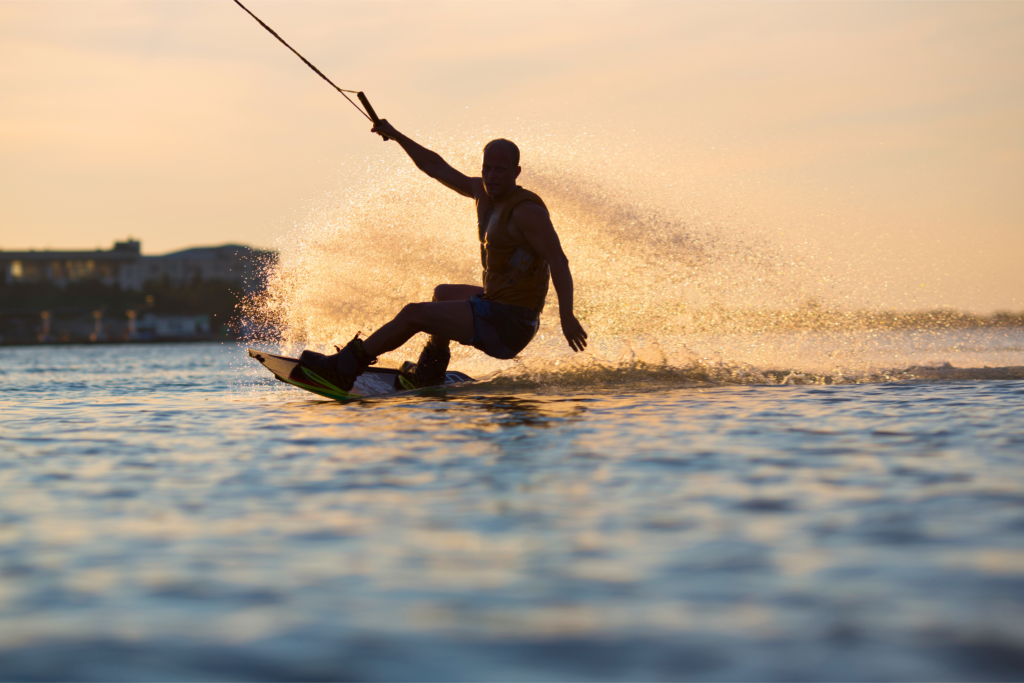 Persona che pratica wakeboard al tramonto trainata da una barca