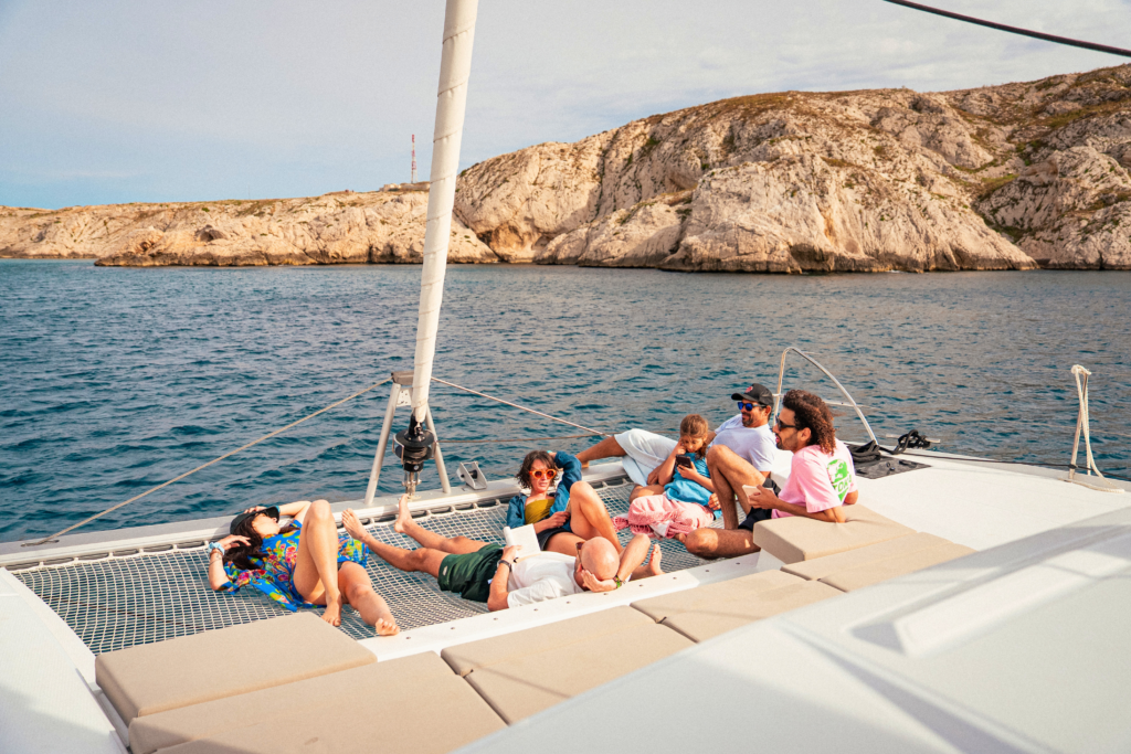 Gruppo di persone che si rilassa a bordo di un catamarano all'ancora vicino a una costa rocciosa