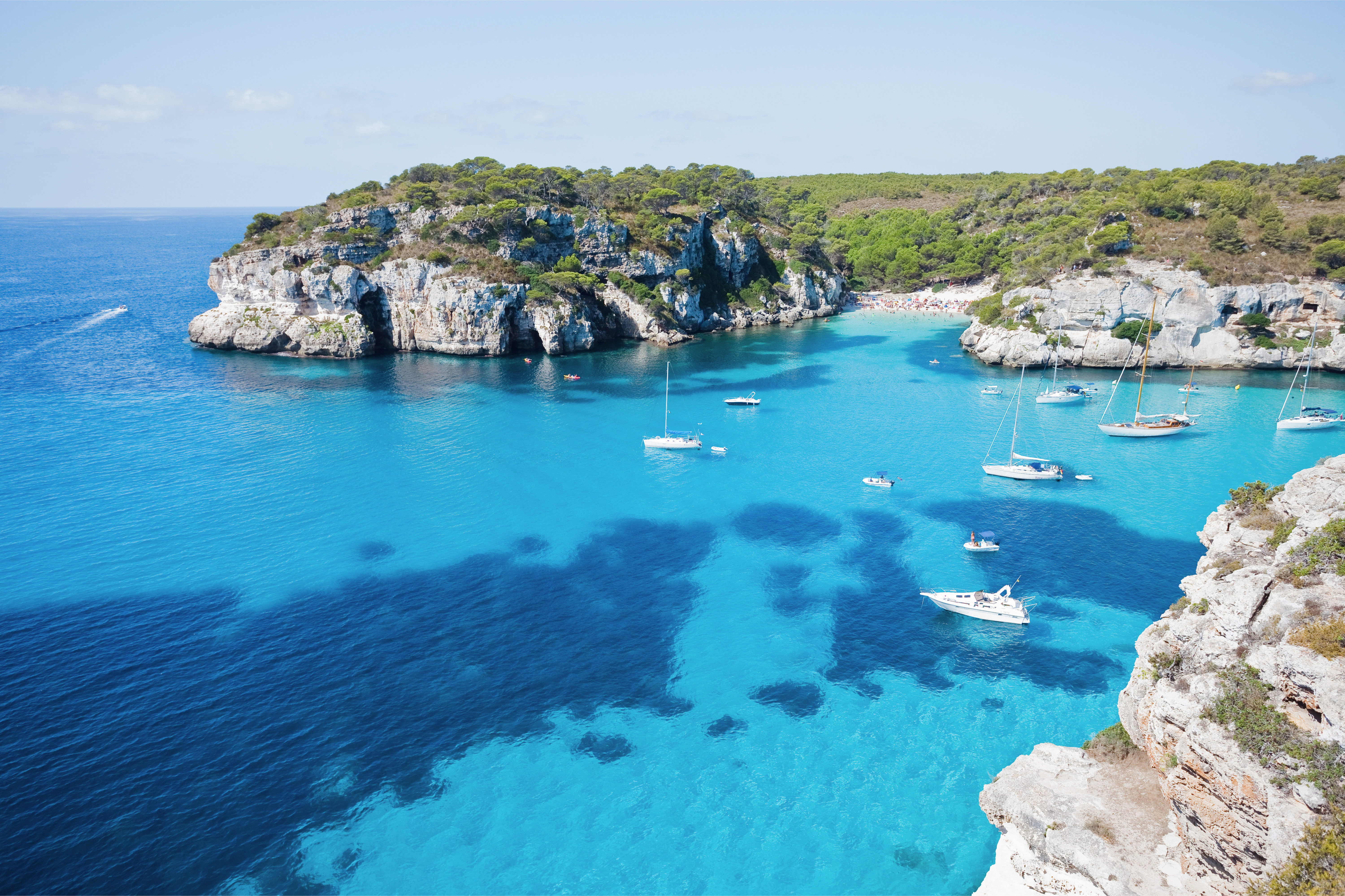 Barche e velieri all'ancora in una cala dalle acque turchesi circondata da scogliere